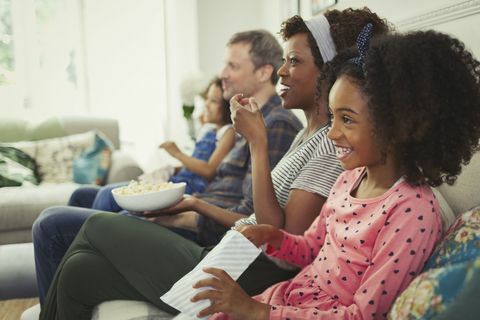 Ung multietnisk familie som ser på film og spiser popcorn på sofaen