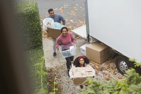 Familie som flytter inn i nytt hus, bærer kasser fra flyttebil