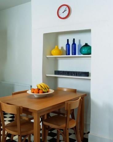 alkoveideer, enkelt trebord og stoler i moderne hvitt kjøkken med svart hvitt sjakkgulv