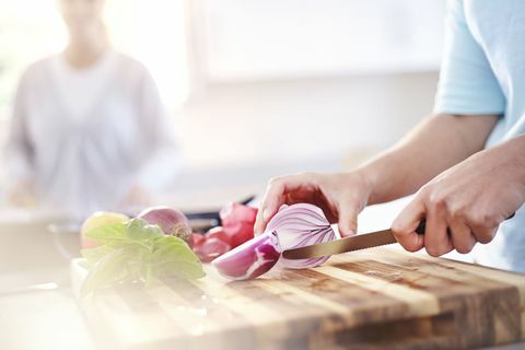 Kvinne, skiver rødløk på skjærebrett på kjøkkenet