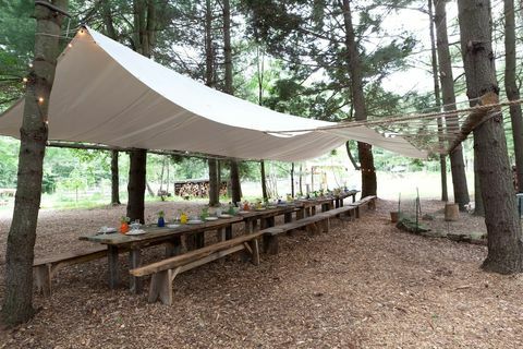 spisestue med strekk av trebord og benker, teltet med presenningslignende materiale festet til trær langs spiseplassen